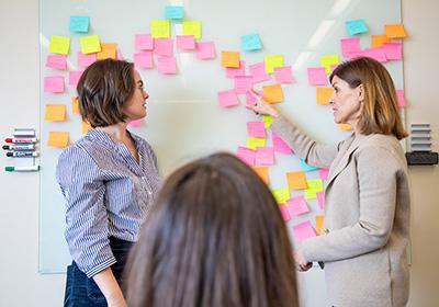 two women discuss various post-it notes on board