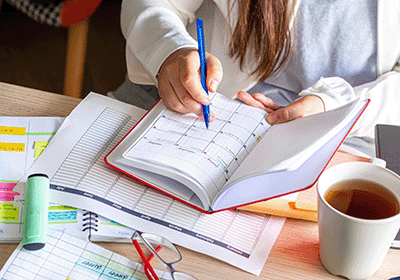 person writing in planner at a cluttered desk
