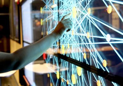 person pointing at complicated digital display on glass board