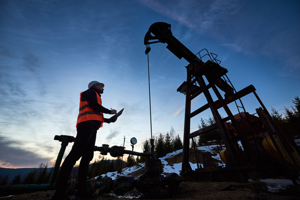 silhouette of field technician and pump jack against clear sky