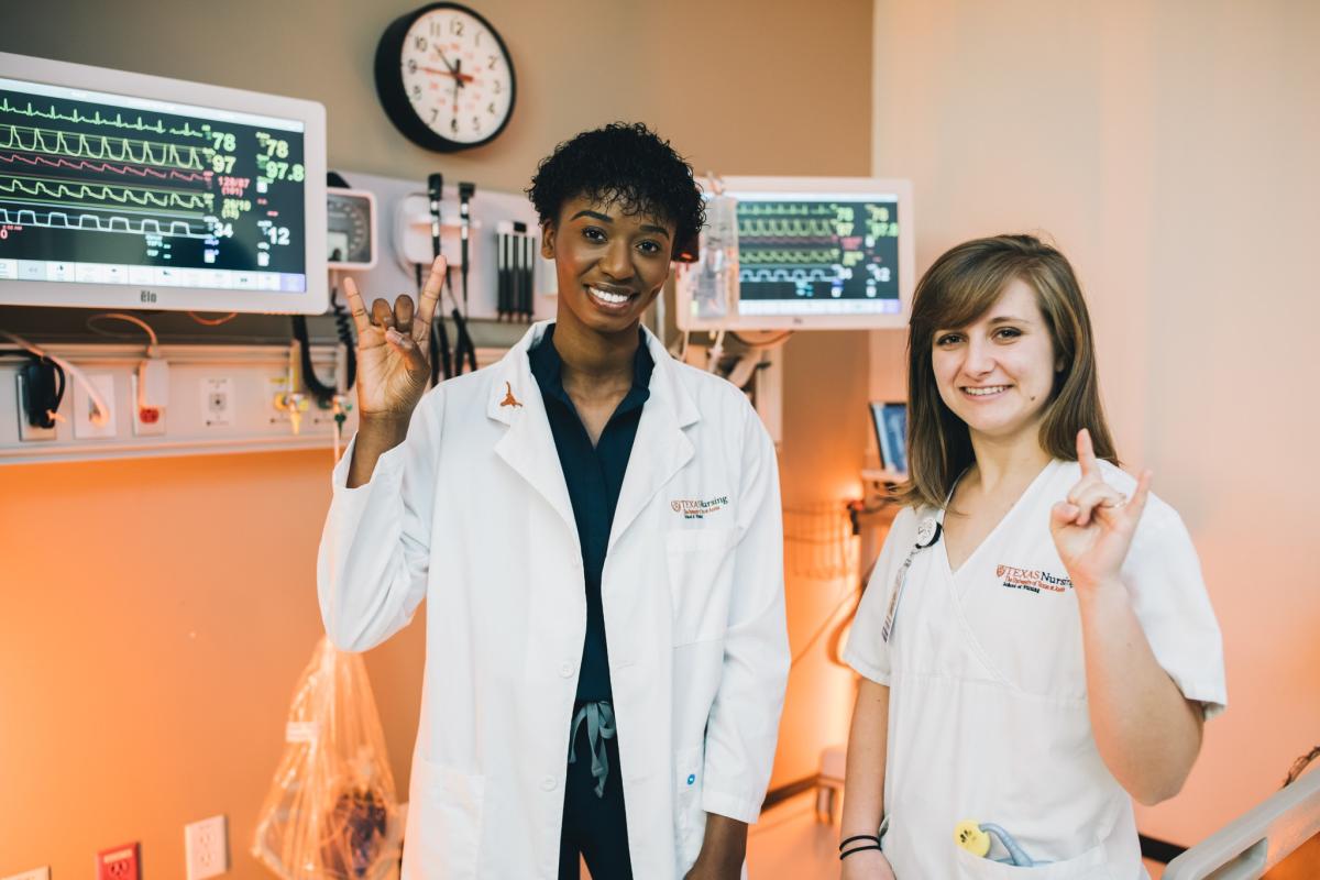 two nursing students in scrubs showing hook 'em sign