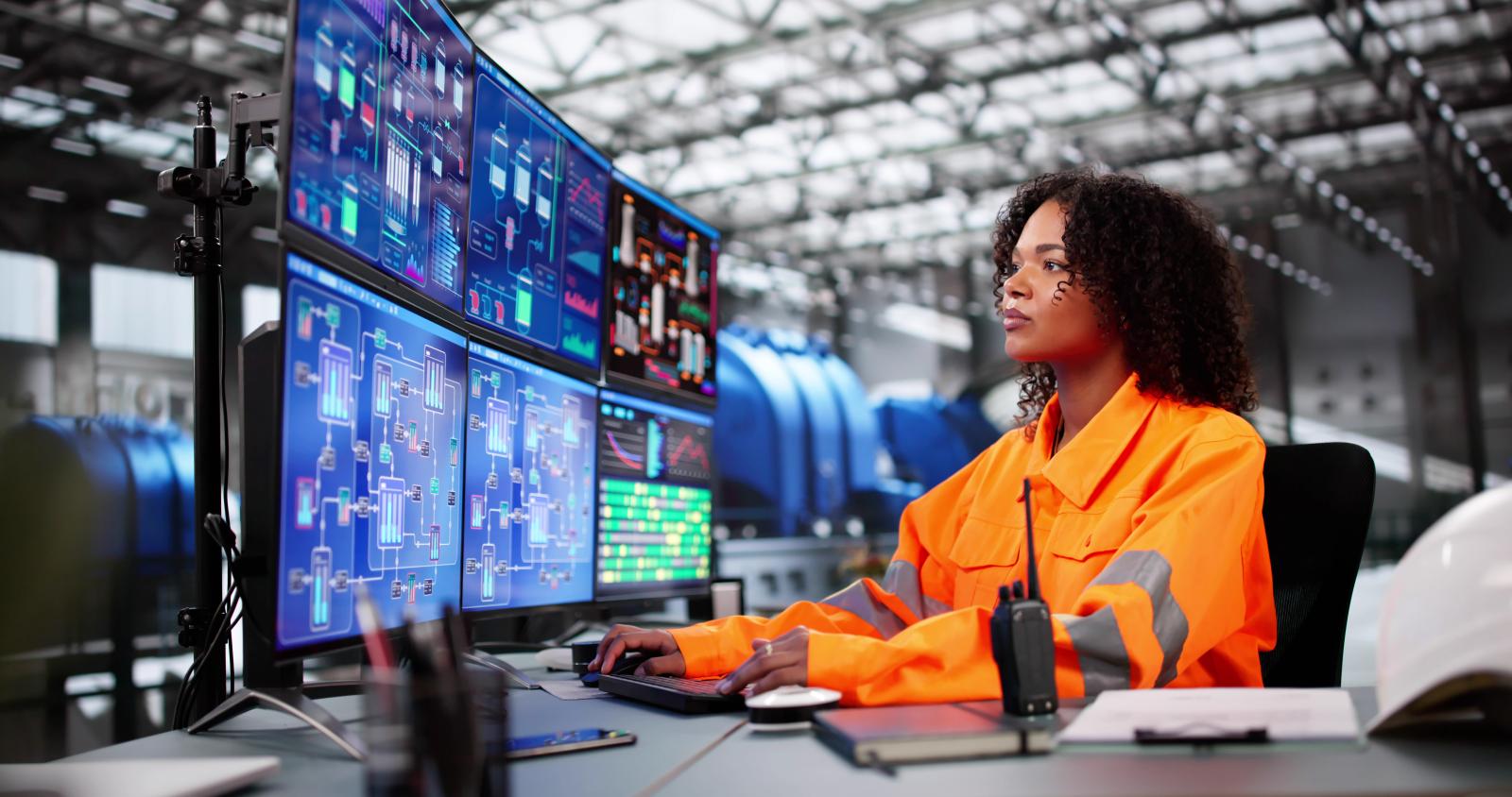 Woman in orange jacket looking at multiple computer screens